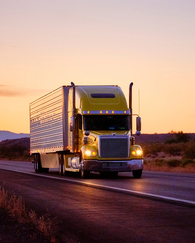 Yellow semi-truck driving down a highway at sunset.
