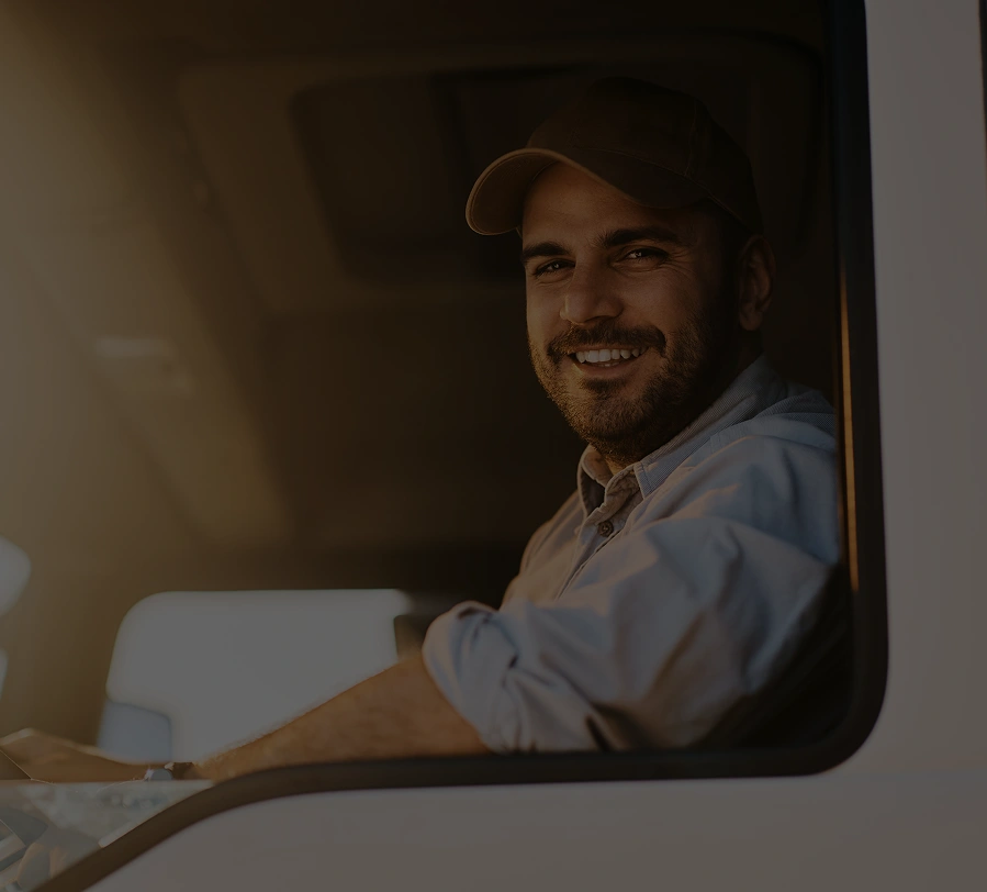 Smiling truck driver sitting in the cab, looking at the camera in warm evening light.